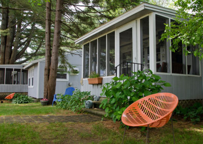 A cottage with a porch and chairs in the yard.