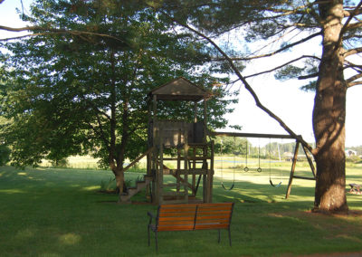 A wooden bench next to a swing set in a field.