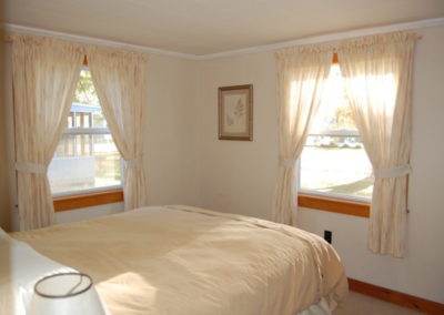 A queen bed in a bedroom with two windows.