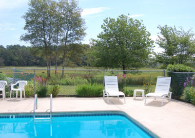 A swimming pool next to a field and marsh.