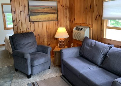 Cottage living room with a sleeper sofa, easy chair and wall-mounted heating and A/C unit.