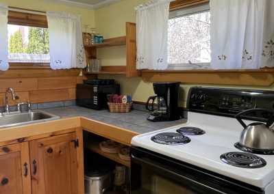 A kitchen with an electric range, coffee pot, microwave, sink and cookware