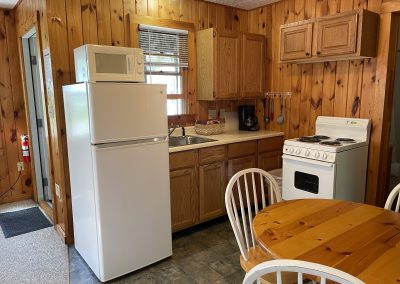 A cottage kitchen with a fridge, apartment-sized range, sink and a dining table with three chairs