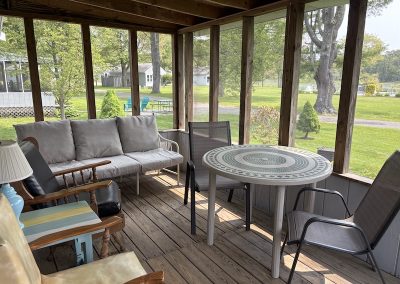 A screened porch on a cottage with a dining table and several easy chairs