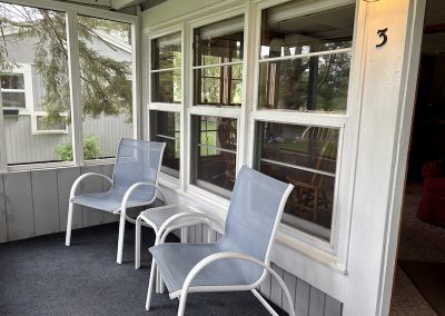A cottage porch with two chairs and a side table