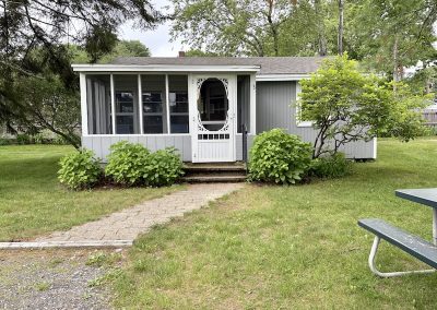 The exterior of a grey cottage with a picnic table in the foreground